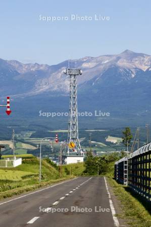 アンテナと防雪柵と固定式視線誘導柱と十勝岳連山